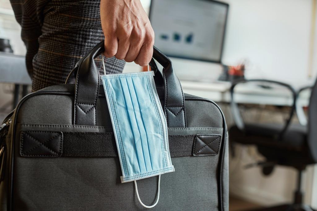 business-skills-BC mans hand holding a black suitcase and disposable mask in the new world of business skills
