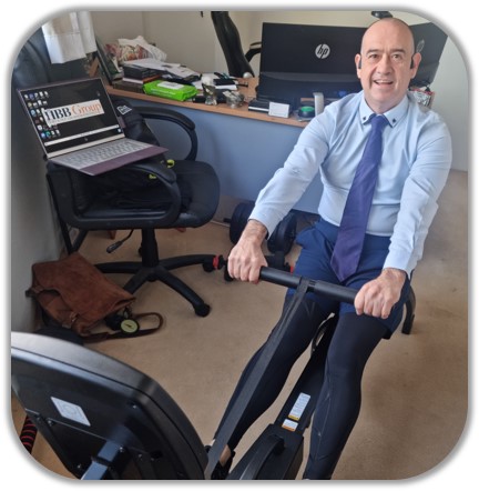 Garret Norris exercising on his rowing machine, half dressed in a shirt and tie and the bottom half in lycra spandex tights for lockdown work from home