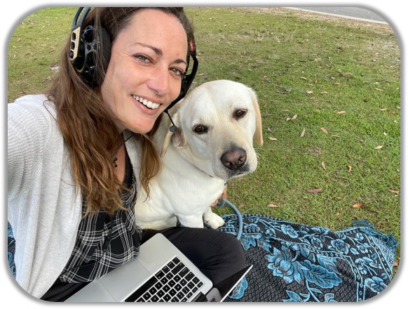 Maud Vanhoutte, KONA's Effective Communication Specialist, with her dog Nalla on a picknic blanket in the park with her laptop